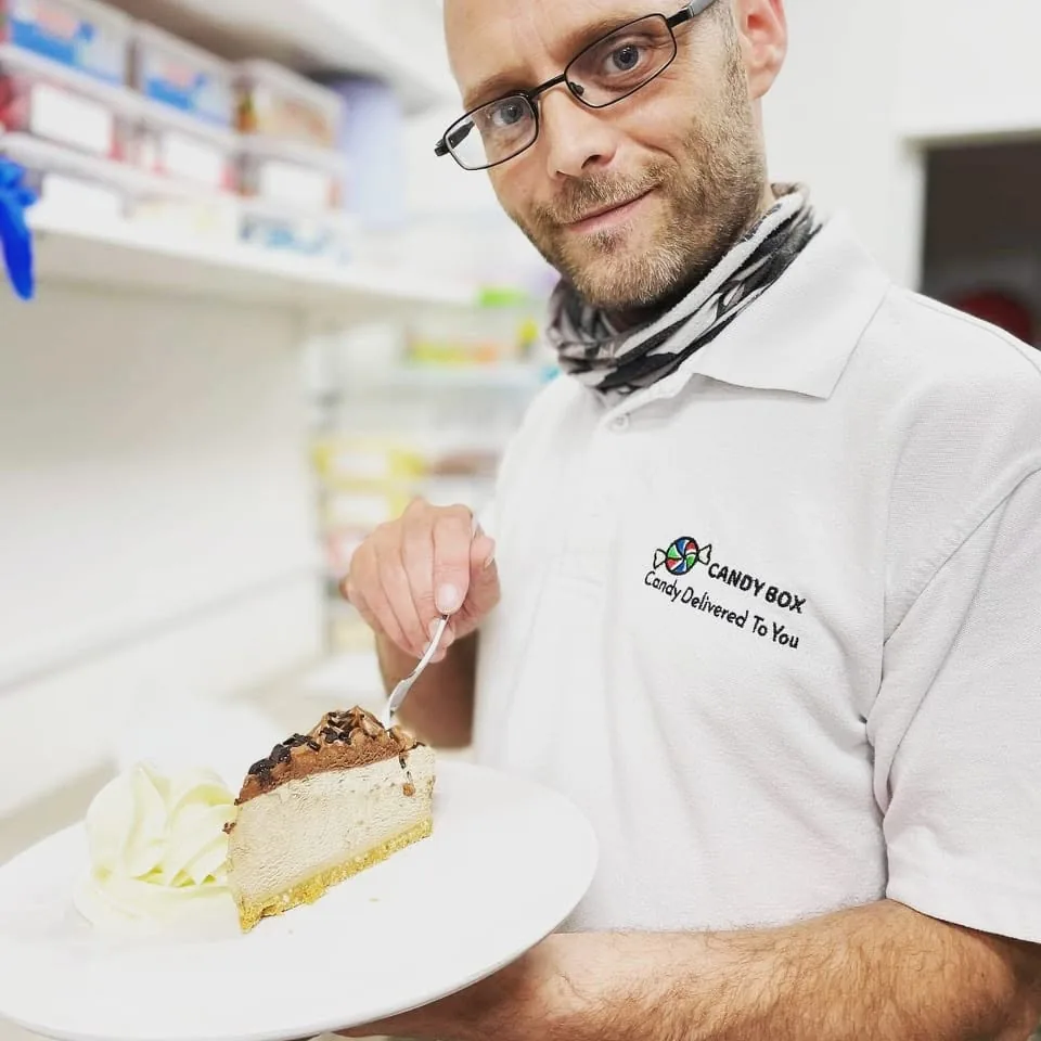 Adam in a Candy Box shirt holding a dessert in the shop